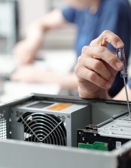 Technician holding screwdriver, repairing computer hardware in laboratory setting, focusing on components inside open computer case